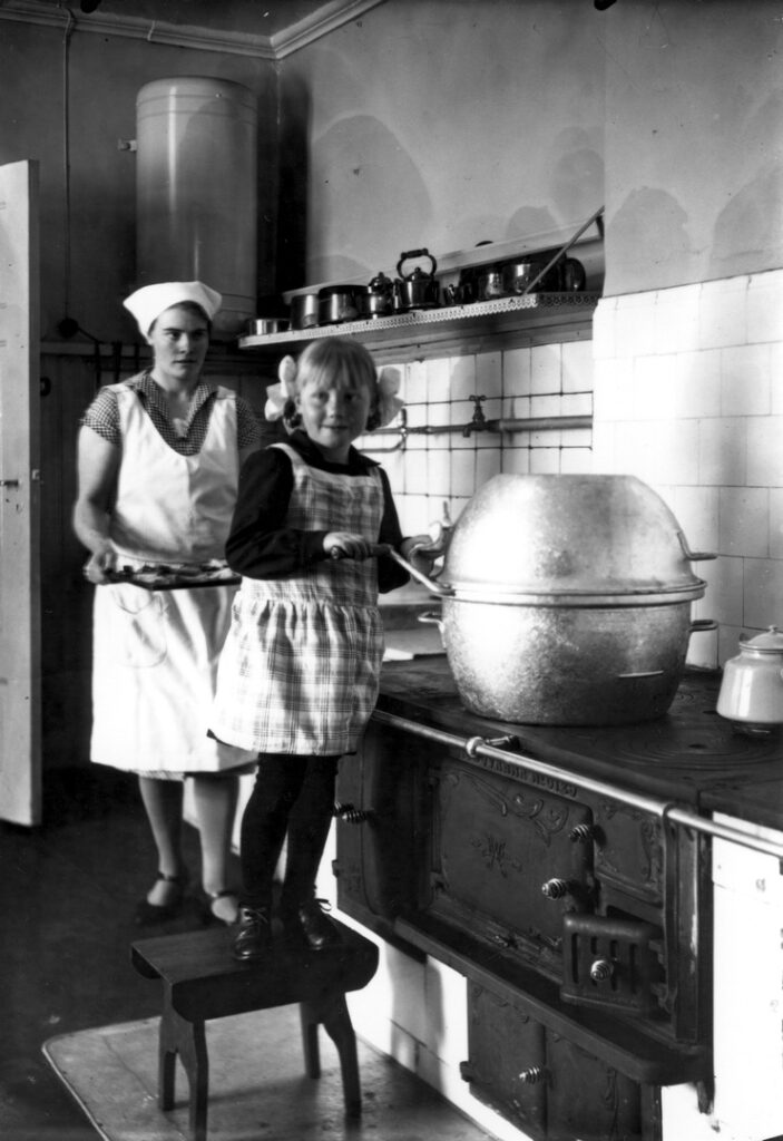 Kök anno cirka 1930. Hembiträdet Anna Paulin och flickan Gurli Runerström, född 1924, i direktörsvillans kök med tvättmaskinen "Tvättkulan".
